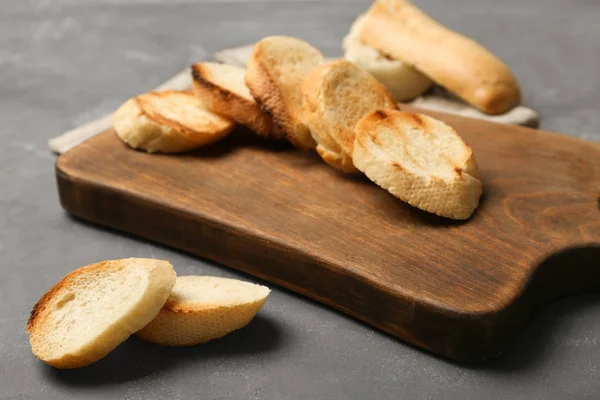 Träskiva med rostat bröd på grå bakgrund — Stockfoto