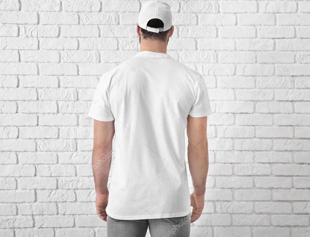 Handsome young man in stylish white t-shirt near brick wall. Mockup for design