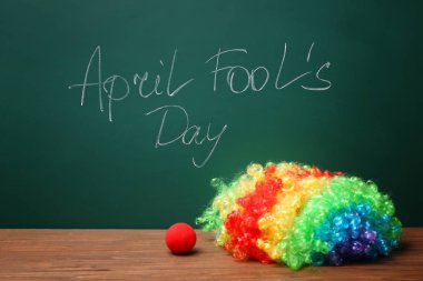 Palyaço burun ve gökkuşağı peruk yakınındaki April fools gün yazılı ifade ile kara tahta masada