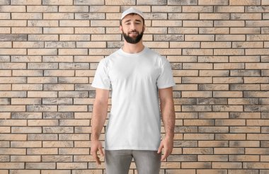 Tuğla duvar yakınındaki şık beyaz t-shirt yakışıklı genç adam. Mockup tasarım için