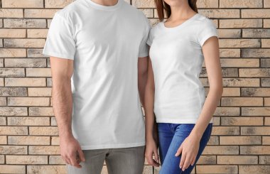 Young man and woman in stylish white t-shirts near brick wall. Mockup for design clipart