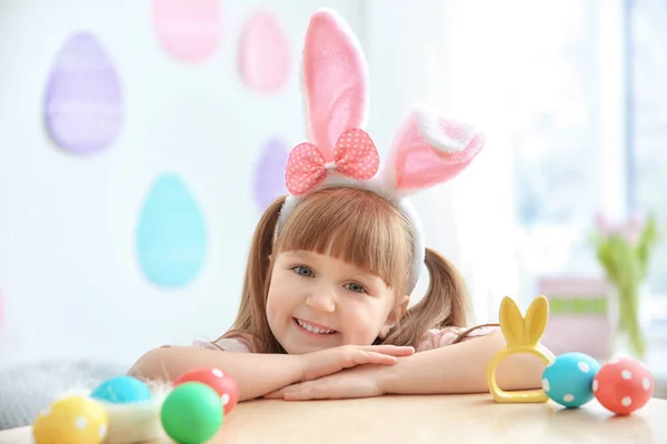 Menina bonito com orelhas de coelho na mesa com ovos de Páscoa — Fotografia de Stock