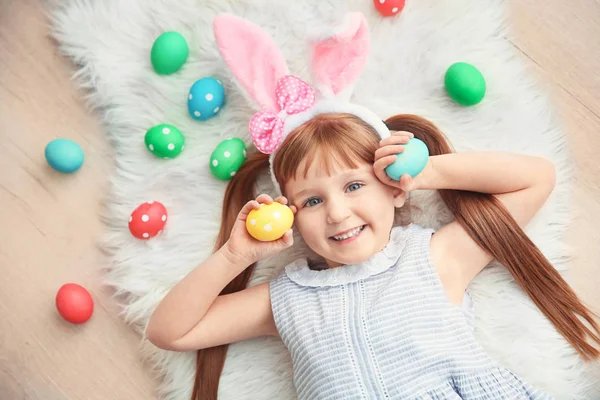 Roztomilá holčička zajíček uši a barevné velikonoční vajíčka leží na podlaze — Stock fotografie