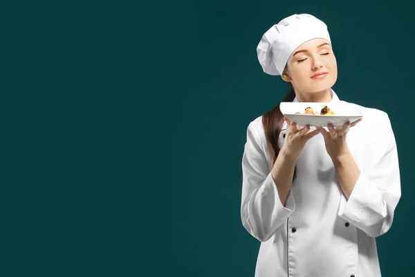 Beautiful female chef holding plate with dish on color background — Stock Photo, Image