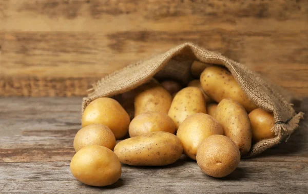 Zak verse rauwe aardappelen op houten tafel — Stockfoto