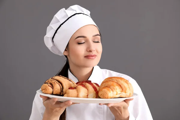 Belo chef feminino segurando prato com croissants no fundo cinza — Fotografia de Stock