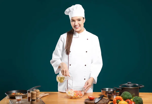 Schöne Köchin, die Salat am Tisch vor farbigem Hintergrund mit Öl würzt — Stockfoto