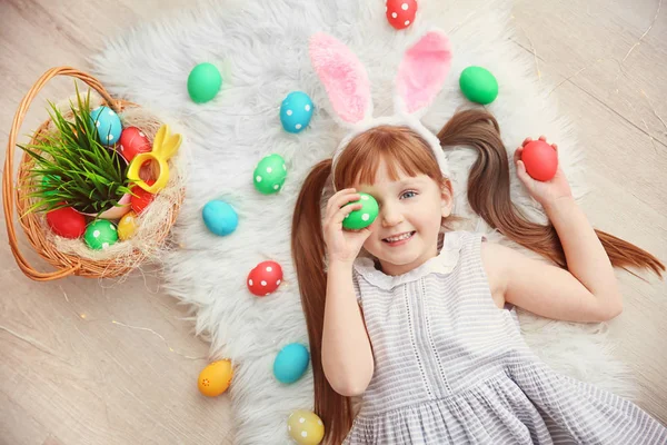 Linda niña con orejas de conejo y coloridos huevos de Pascua tirados en el suelo —  Fotos de Stock