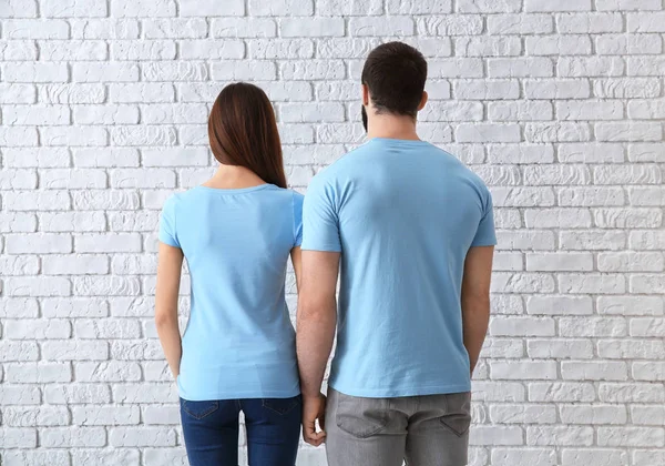 Ung man och kvinna i snygga t-shirts nära vit tegelvägg. Mockup för design — Stockfoto