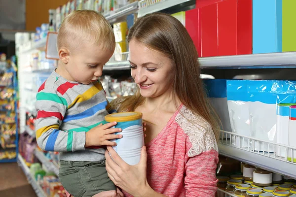 Jonge moeder met kleine zoon kiezen van babyvoeding in de supermarkt — Stockfoto