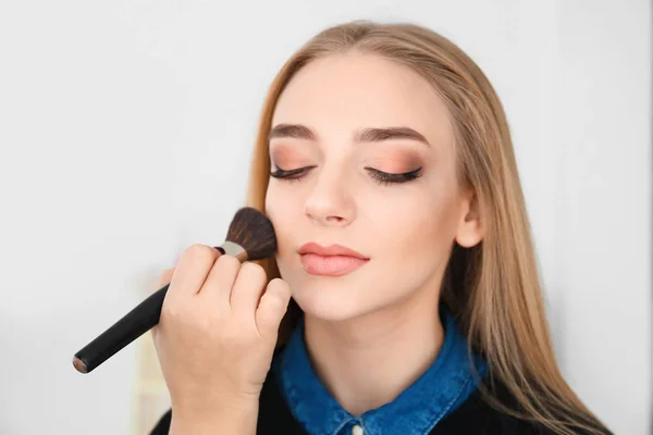 Professional visage artist applying makeup on woman's face against light background — Stock Photo, Image