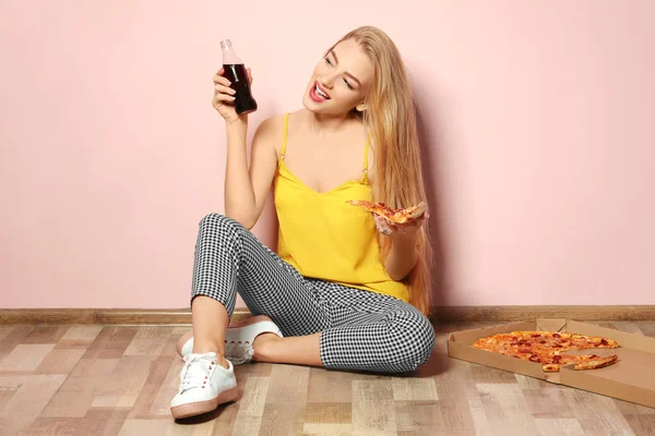 Atractiva chica hipster con sabrosa pizza y botella de cola cerca de la pared de color —  Fotos de Stock