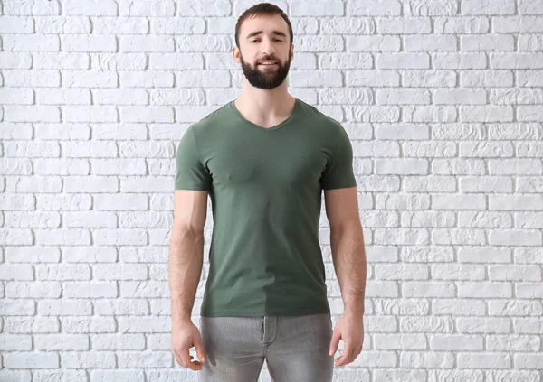 Young man in stylish t-shirt near white brick wall. Mockup for design