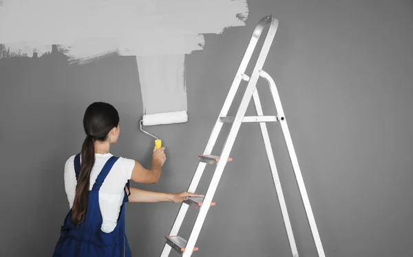 Декоратор окрашивает серую стену в белый цвет с помощью ролика — стоковое фото