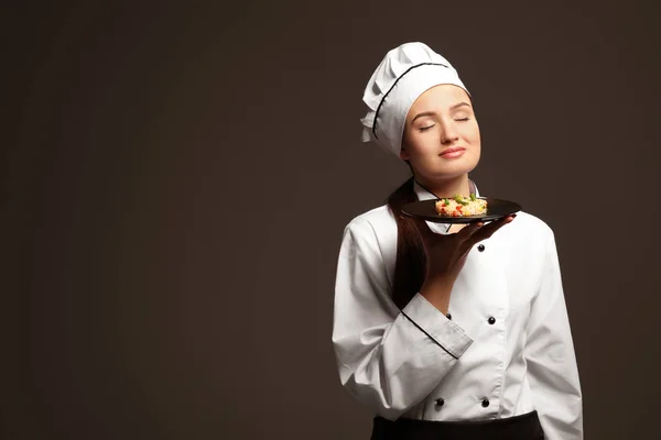 Beautiful female chef holding plate with dish on dark background — Stock Photo, Image