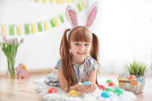 Menina bonito com orelhas de coelho segurando ovo de Páscoa brilhante dentro de casa — Fotografia de Stock