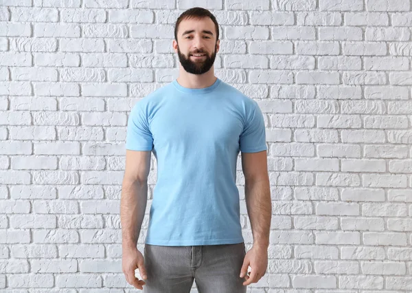 Young man in stylish t-shirt near white brick wall. Mockup for design — Stock Photo, Image