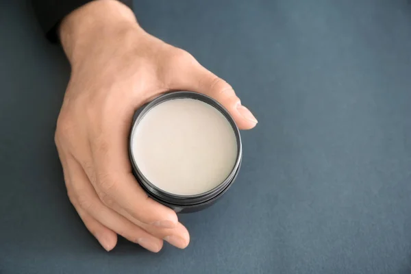 Mão masculina segurando frasco com argila para o cabelo no fundo cinza — Fotografia de Stock