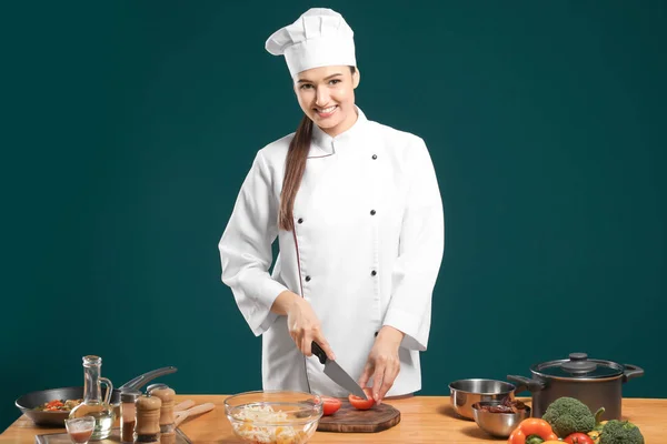 Belo chef feminino cortando tomate na mesa contra fundo de cor — Fotografia de Stock