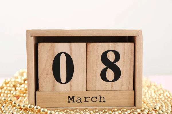 Drewniany klocek kalendarza i złote koraliki na stole. Obchody dnia kobiet — Zdjęcie stockowe