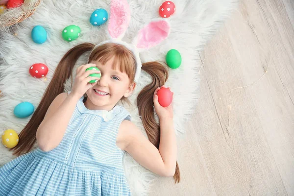Carina bambina con orecchie da coniglio e uova di Pasqua colorate sdraiato sul pavimento — Foto Stock