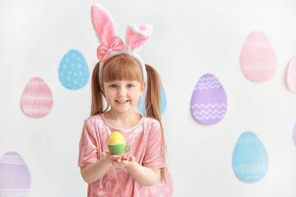 Menina bonito com orelhas de coelho segurando ovo de Páscoa brilhante dentro de casa — Fotografia de Stock