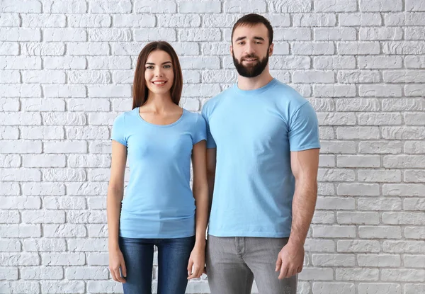 Giovane uomo e donna in eleganti t-shirt vicino al muro di mattoni bianchi. Mockup per il design — Foto Stock