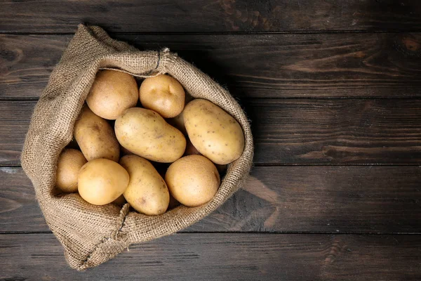 Sack of fresh raw potatoes on wooden background, top view — Stock Photo, Image