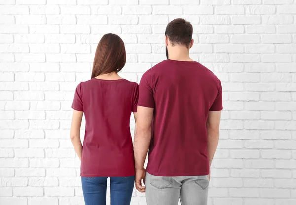 Young man and woman in stylish t-shirts near white brick wall. Mockup for design