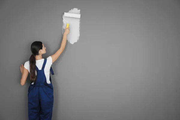 Декоратор окрашивает серую стену в белый цвет с помощью ролика — стоковое фото
