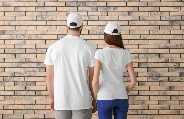 Young man and woman in stylish white t-shirts near brick wall. Mockup for design