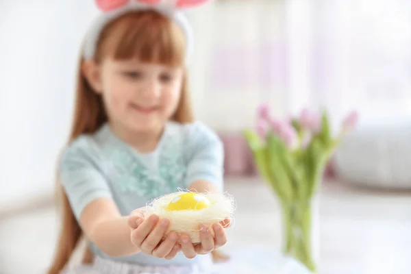 Menina bonito com orelhas de coelho segurando ovo de Páscoa brilhante em ninho decorativo, dentro de casa — Fotografia de Stock