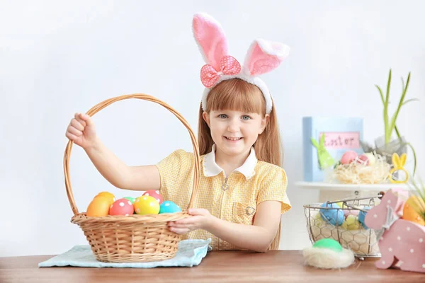 Aranyos kis lány, nyuszi füle bent tartja a kosár tele színes húsvéti tojás — Stock Fotó