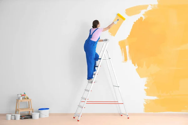 Decorador pintura parede branca na cor amarela com rolo — Fotografia de Stock