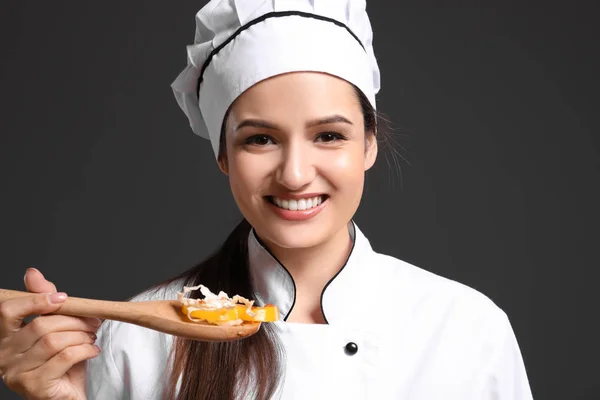 Vackra kvinnliga kock holding träsked med sallad på mörk bakgrund — Stockfoto