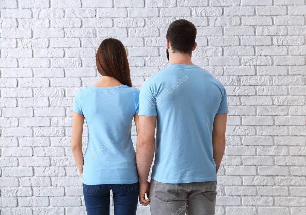 Young man and woman in stylish t-shirts near white brick wall. Mockup for design