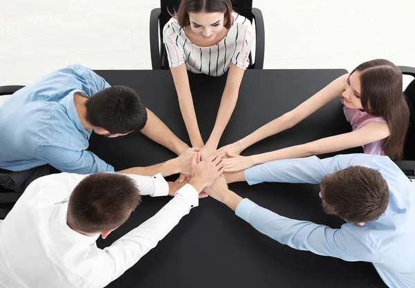 Young people putting hands together at table, indoors. Unity concept — Stock Photo, Image
