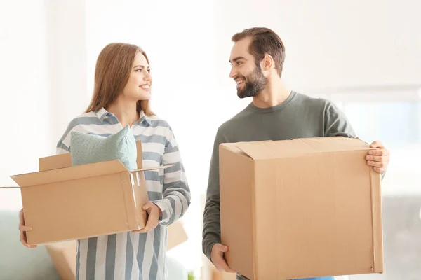 Young couple with moving boxes in room at new home — Stock Photo, Image