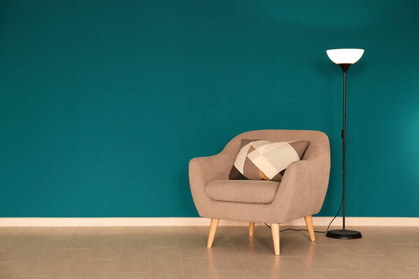 Trendy armchair with lamp near shaded spruce wall