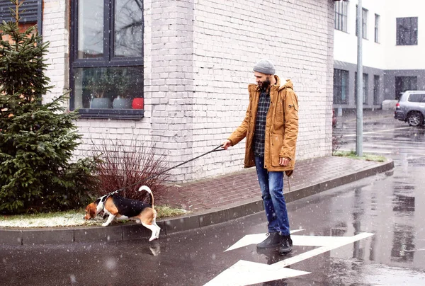 Beau jeune hipster promenant son chien à l'extérieur le jour neigeux — Photo