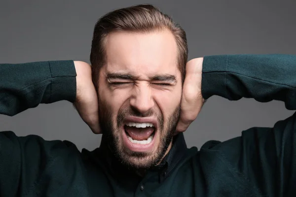 Joven con problemas auditivos cubriendo oídos sobre fondo gris —  Fotos de Stock