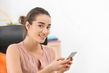 Young woman with hearing aid using smartphone indoors