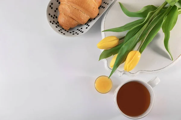 Piring dengan croissant, secangkir teh dan bunga di atas meja, pemandangan atas. Sarapan lezat — Stok Foto