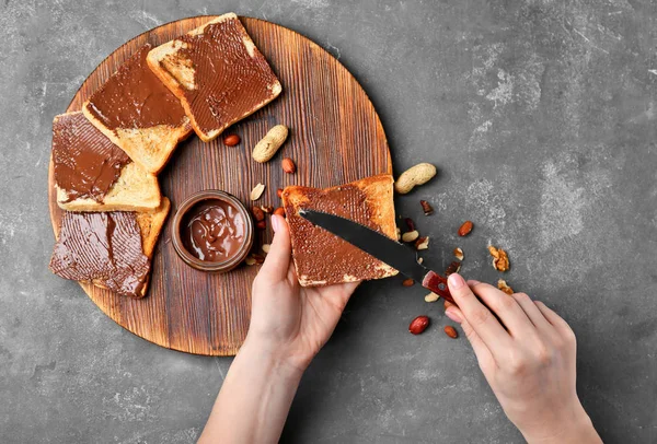 Wanita menyebarkan pasta coklat pada roti panggang di atas meja, pemandangan yang bagus — Stok Foto