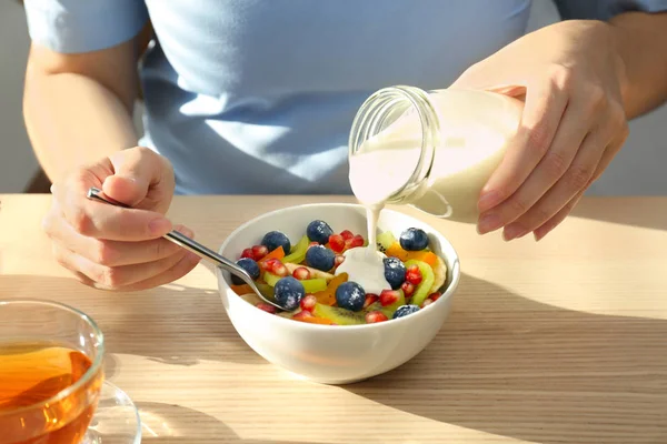 Mujer vertiendo sabroso yogur sobre las frutas en un tazón en la mesa —  Fotos de Stock