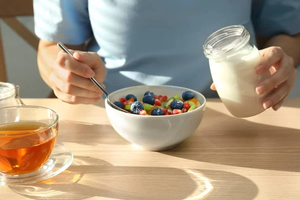 Mujer comiendo frutas con sabroso yogur en la mesa — Foto de Stock