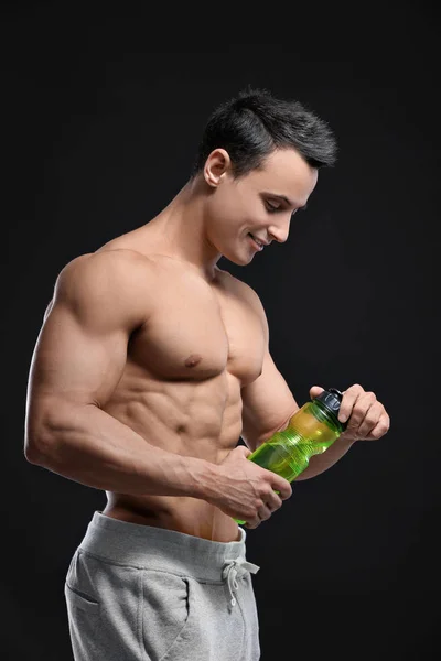 Przystojny mięśni młody człowiek z butelka wody na czarnym tle — Zdjęcie stockowe