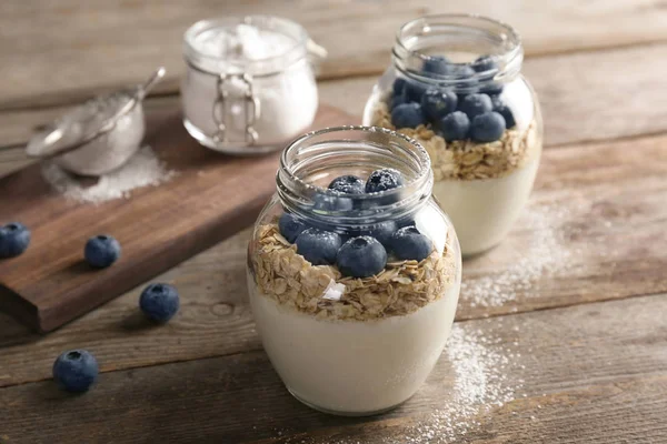 Yogurt with oat flakes and blueberry in jars on wooden table — Stock Photo, Image