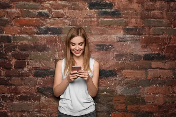 Mulher bonita com telefone celular perto da parede de tijolo — Fotografia de Stock