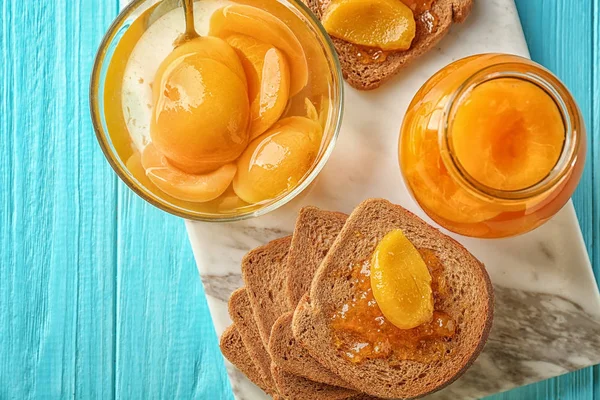 Rebanadas de pan, tazón y frasco con albaricoques en escabeche en la mesa — Foto de Stock